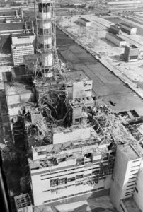 Foto aérea em preto e branco do Reator 4 da Usina de Chernobyl após a explosão. O edifício industrial exibe danos estruturais massivos, telhado destruído e escombros espalhados ao redor da torre de ventilação.