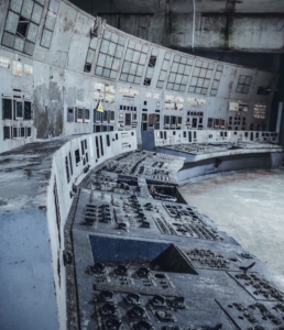 A sala de controlo do Reator 4 encontra-se completamente destruída e abandonada. Os longos painéis curvos de operação estão cobertos de poeira e ferrugem, sem botões nem instrumentos funcionais. As paredes curvas do fundo mostram estruturas metálicas expostas e sinais graves de degradação.