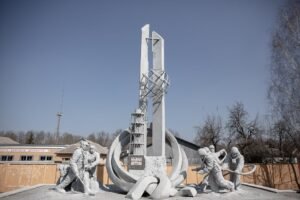 Monumento "Àqueles que Salvaram o Mundo", dedicado aos bombeiros e liquidadores de Chernobyl. Ao centro, erguesse um pilar cinzento com uma cruz e um globo armilar, cercado por aneis de concreto e uma maquete do reator. Nas laterais, esculturas de bombeiros e trabalhadores parecem atuar no combate ao desastre sob um céu limpo.